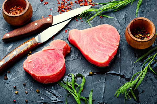 Fresh Albacore tuna on a slate grey cutting board with scallions and sushi-cutting knives